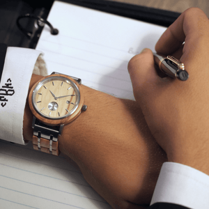 Person wearing wooden and metal watch while writing